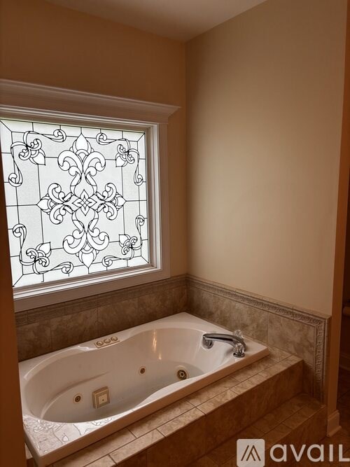 A bathroom with a tub and a window with a decorative glass.