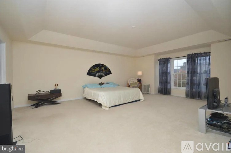 A bedroom with a bed, two TVs, and a window with curtains.
