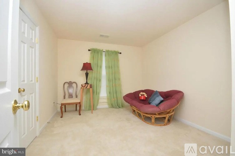 A room with a white door, a green curtain, a red lamp, a wooden chair, and a wicker chair with a red cushion.