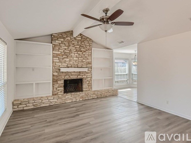 A living room with a stone fireplace and a ceiling fan.