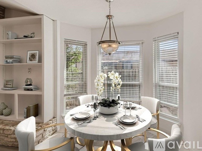 A dining room with a round table set for two and a chandelier hanging from the ceiling.