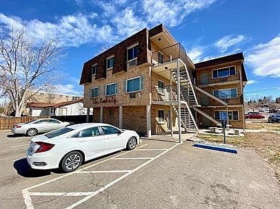 A white car is parked in a parking lot in front of a two-story building.