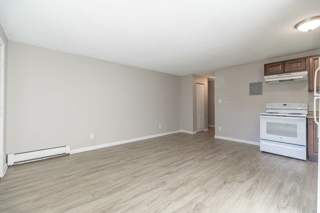 A spacious room with light wood flooring and a white kitchenette.