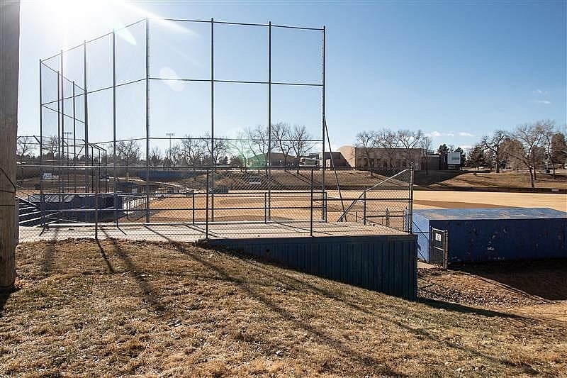 A tennis court with a fence and a building in the background.