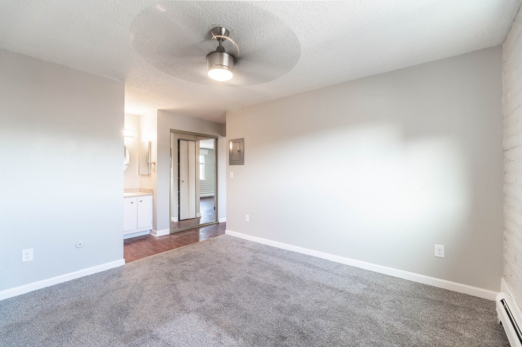 A spacious room with a grey carpet and a ceiling fan.