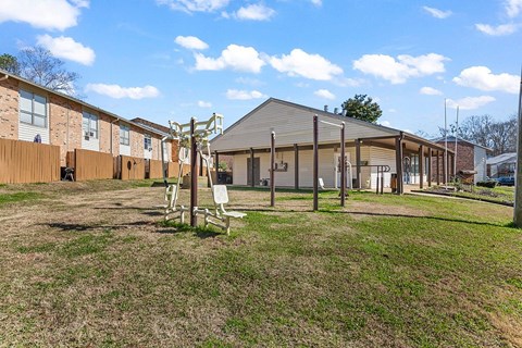 A playground with a swing set in the middle of a grassy area in front of a building.