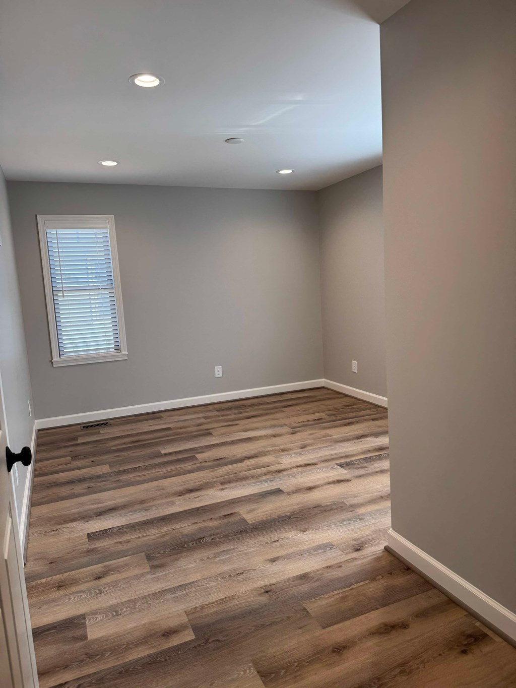 A room with wooden flooring and a window with blinds.