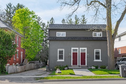 A grey house with a red door stands on a street.