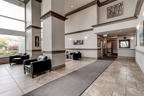 A large, well-lit lobby with a grey carpet and a row of black chairs.