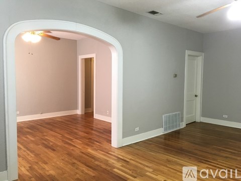 A room with wooden floors and white walls, with a doorway leading to another room.