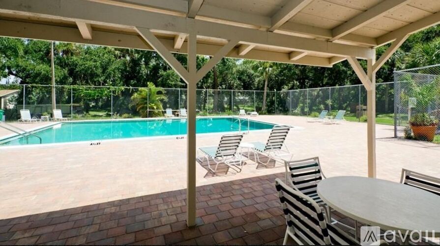 A covered patio area with a table and chairs overlooking a pool.