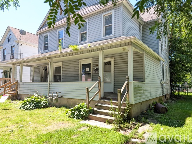 A house with a grey and white exterior is shown with a front yard and a sidewalk.