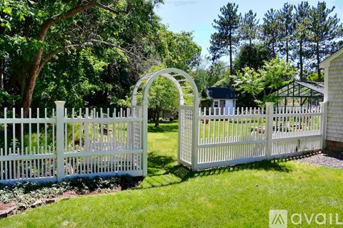 A white fence with a gate stands in a grassy area.