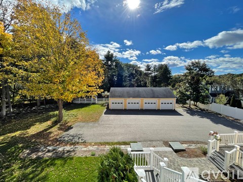 A house with a thatched roof is surrounded by trees and has a driveway leading to the garage.
