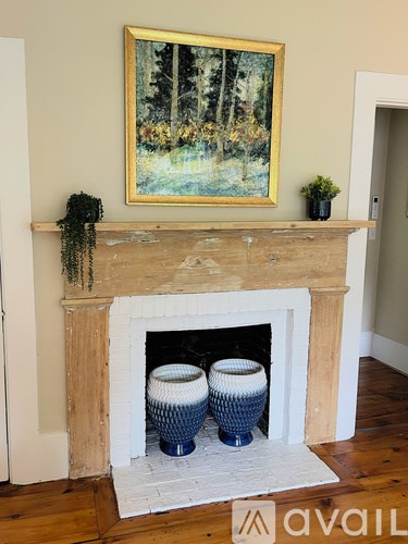 A fireplace with a painting above it and two vases on the hearth.