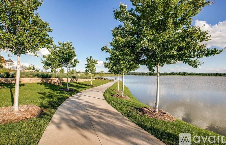 A walkway with trees on either side leads to a body of water.