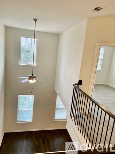 A living room with a ceiling fan and a balcony with a railing.