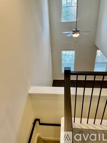 A staircase with a wooden handrail and a fan in the background.