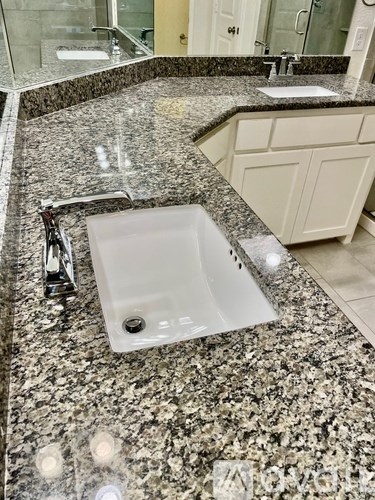 A bathroom sink with a granite countertop and a white cabinet.