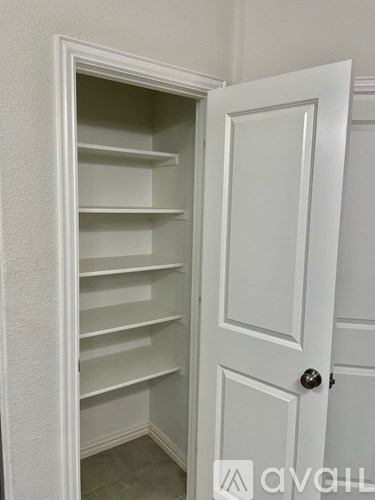 A white door with a black handle is open to a white pantry with shelves.