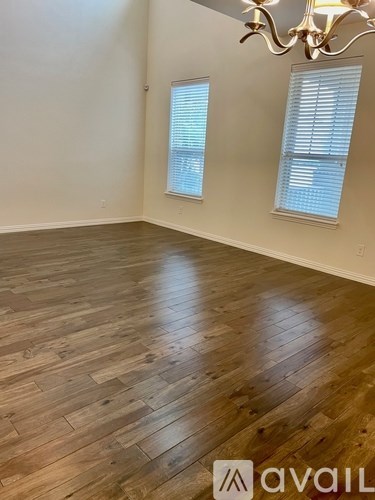 A room with wooden flooring and two windows with blinds.