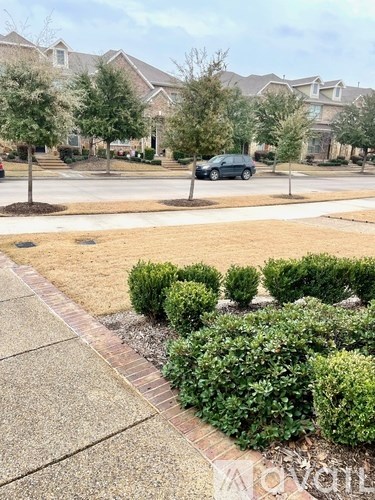 A black car is parked on a street with a sidewalk and a hedge.