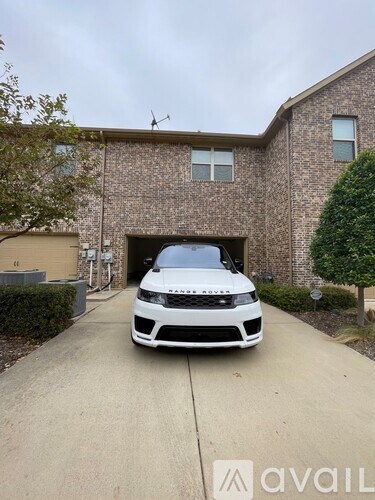 A white car is parked in front of a brick house.