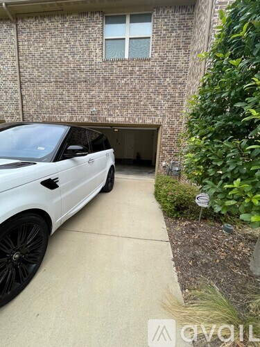 A white car is parked in a driveway next to a brick building.