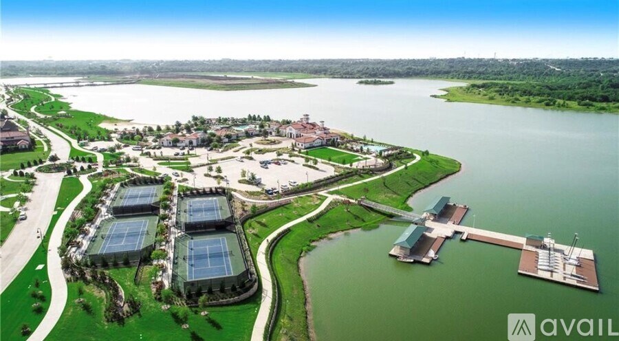 A large building complex with tennis courts is surrounded by water and greenery.