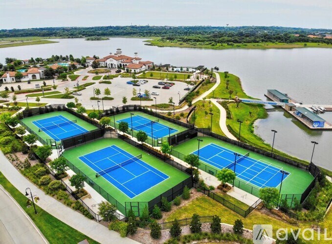 A tennis court complex with multiple courts and a lake in the background.