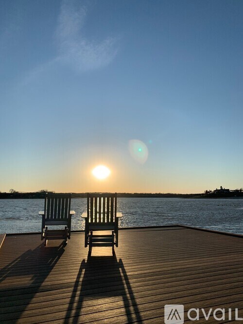 Two chairs are on a dock with the sun setting in the background.