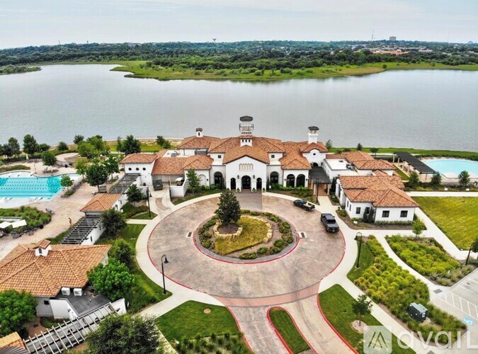 A large white building with a red roof is surrounded by a circular driveway and a lake in the background.