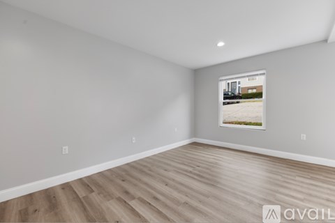 A room with wooden flooring and a window showing a parking lot outside.