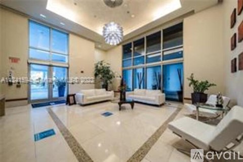 A spacious living room with a white sofa set and a chandelier hanging from the ceiling.
