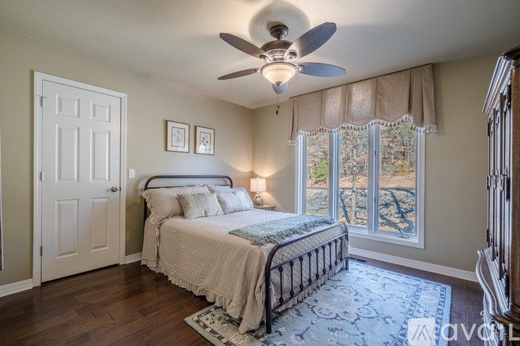 A bedroom with a bed, a ceiling fan, and a window with a view of trees.