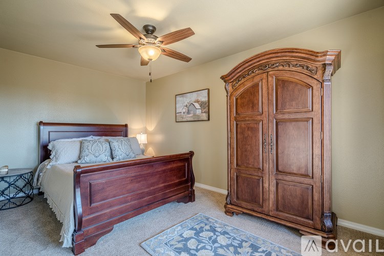 A bedroom with a bed, a ceiling fan, and a wooden armoire.