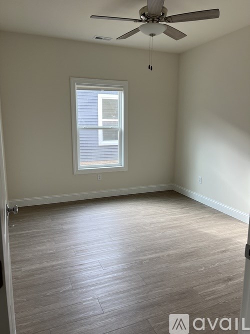 A room with a ceiling fan and light, hardwood floors, and a window with blinds.