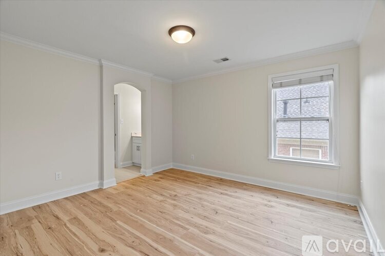 A room with wooden flooring and a window with a view of a building.