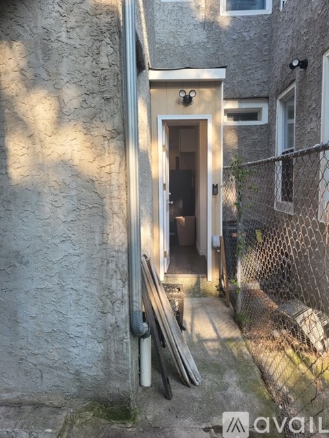 A small doorway in a grey building with a metal fence on the right side.