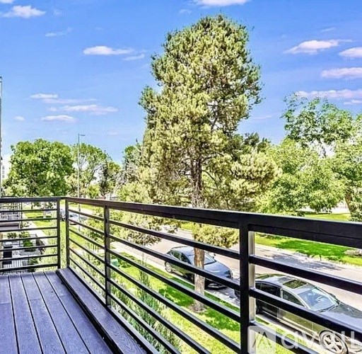 A balcony with a railing overlooks a parking lot and trees.