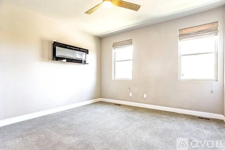 A room with a fan, a window and a wall mounted television.