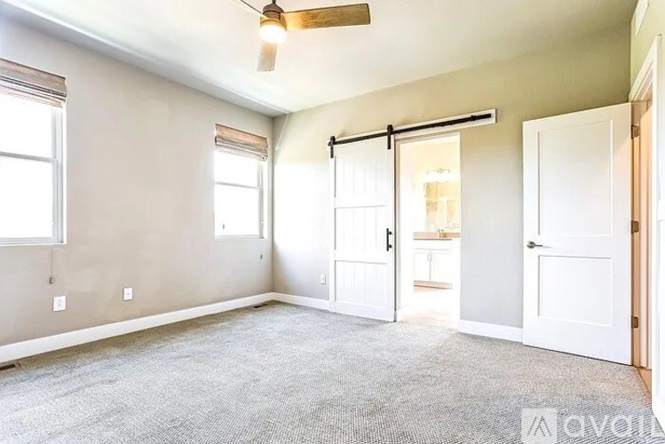 A room with a carpeted floor, a ceiling fan, and a sliding door leading to another room.