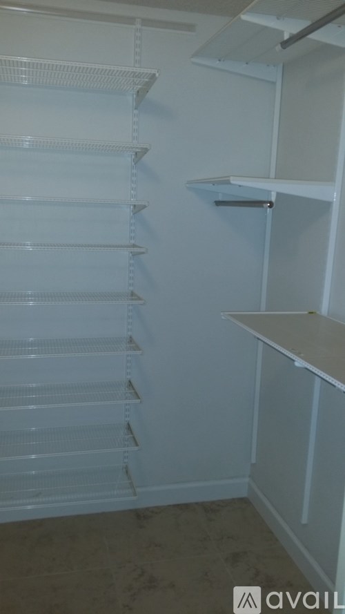 A white empty pantry with a white fridge and white shelves.