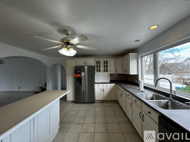 A kitchen with a fan on the ceiling and a refrigerator in the middle.