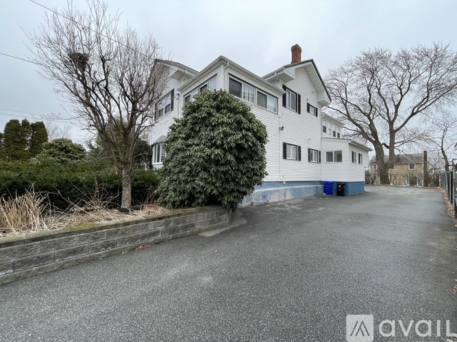 A white house with a blue door is surrounded by a grey wall and trees.
