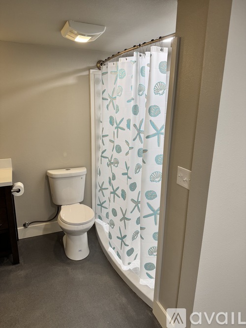 A bathroom with a toilet, a shower curtain with sea creatures on it, and a shower head.