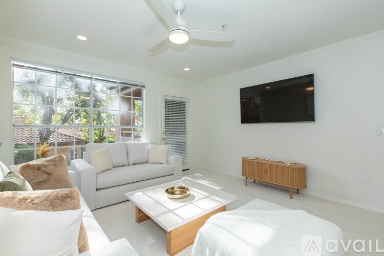 A living room with a white couch, a wooden coffee table, and a flat-screen TV mounted on the wall.