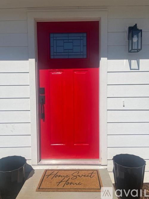 A red door with a glass panel and a doormat that says "Home Sweet Home".