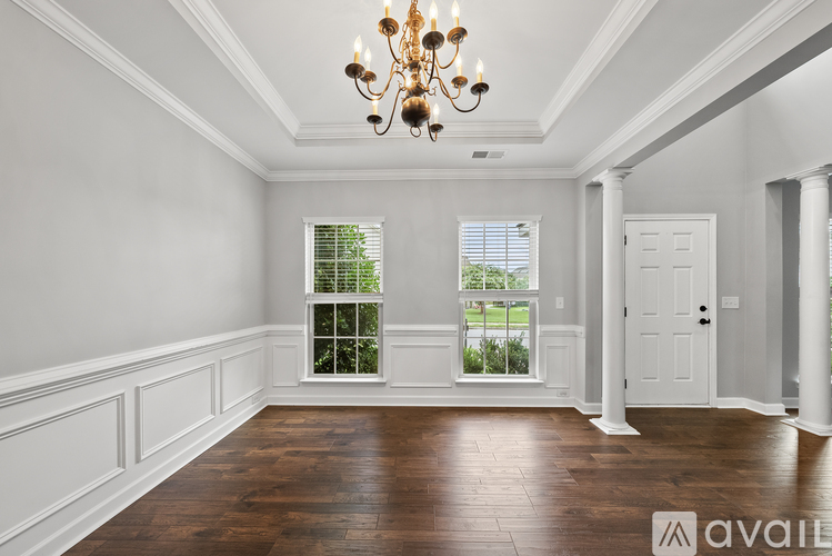 A large, empty room with a chandelier and a view of greenery outside the window.