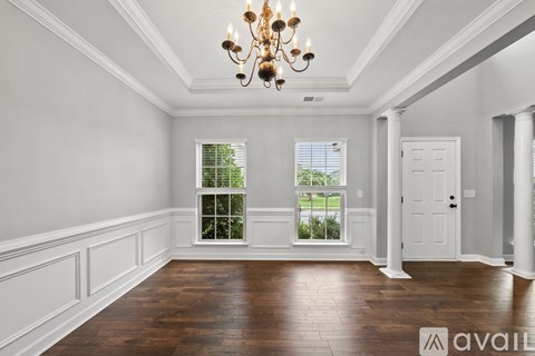 A large, empty room with a chandelier and a view of greenery outside the window.